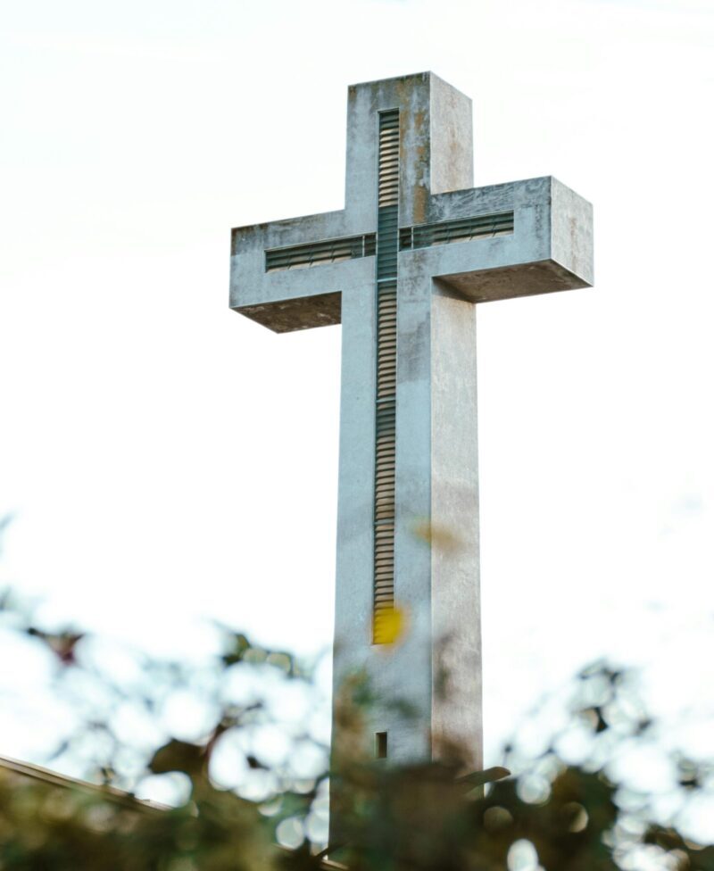 Tall concrete cross surrounded by foliage in Chillán, Chile under a bright sky.